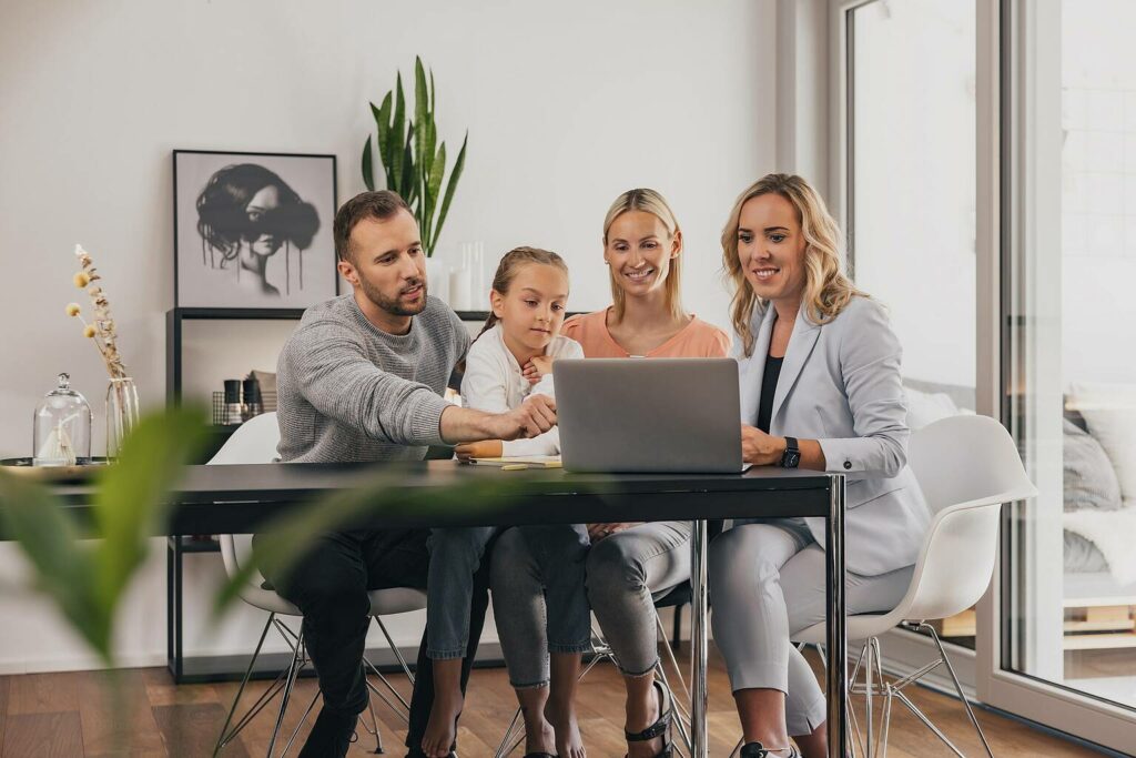 Digitale Plattformen. Das Bild zeigt eine Familie und eine Beraterin, die sich gemeinsam Immobilien online am Laptop anschauen. 